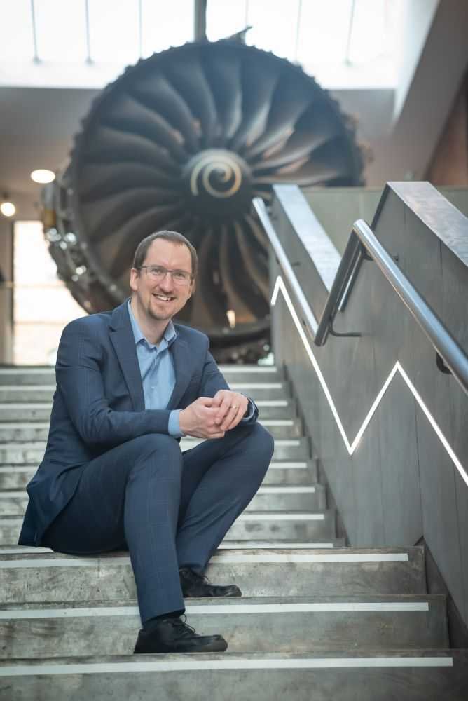 Mike Cole sat on steps in front of a Rolls-Royce engine